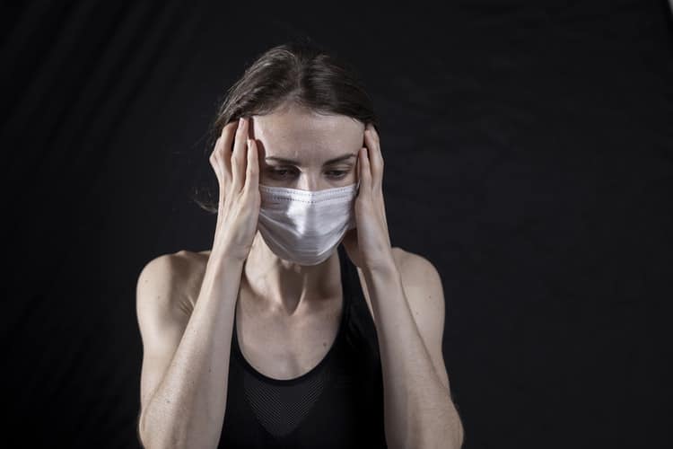 Woman in mask holds her head.