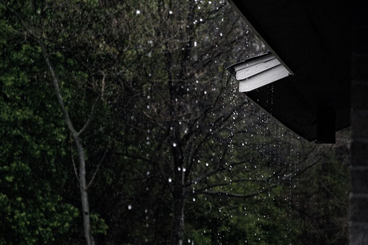 Rain falling from the sky and dripping off a house gutter.