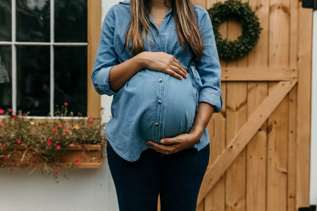 A pregnant woman standing in front of a house.