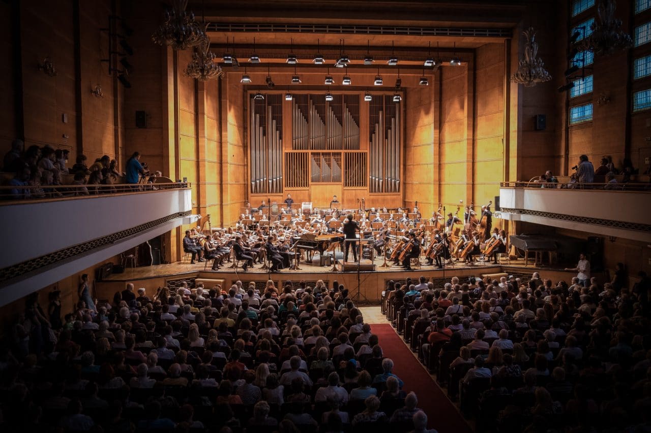 A packed concert venue with a symphony orchestra playing.