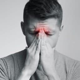 Sinus pain, sinusitis. Sad man holding his nose, black and white photo with red sore zone