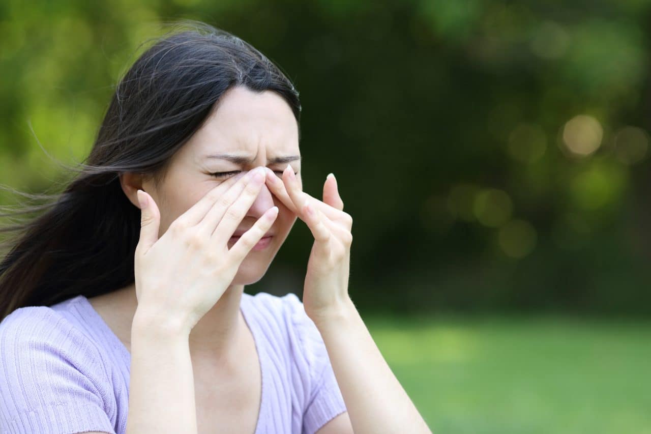 A woman outdoors experiences allergies.