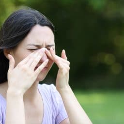 A woman outdoors experiences allergies.