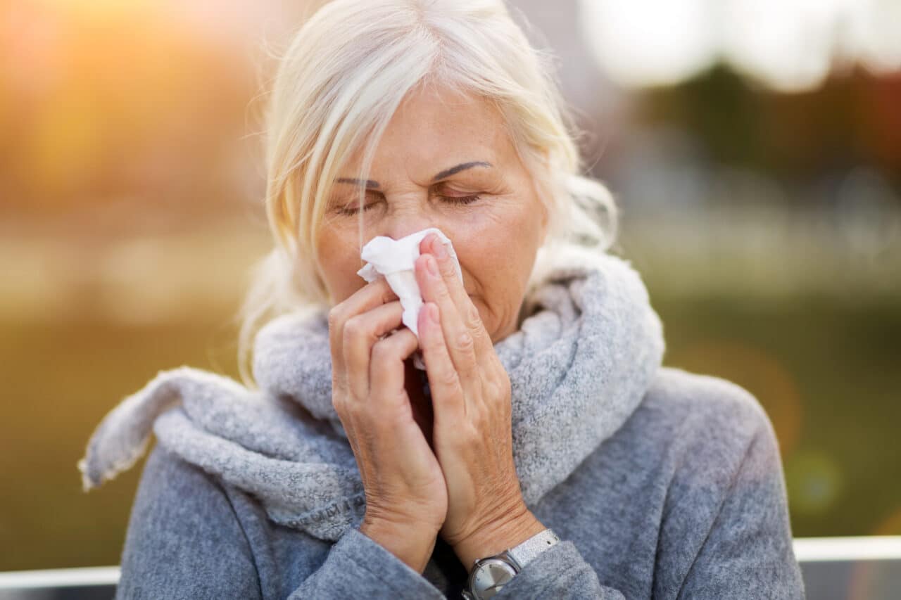 Older woman with allergies blowing her nose.
