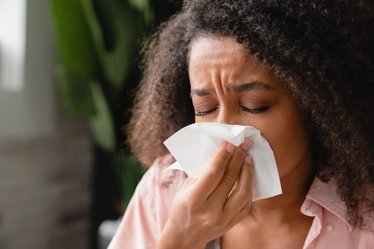 Sneezing coughing ill young african woman using paper napkin, having runny nose, blowing her nose. Coronavirus, infectious disease, flu, cold.