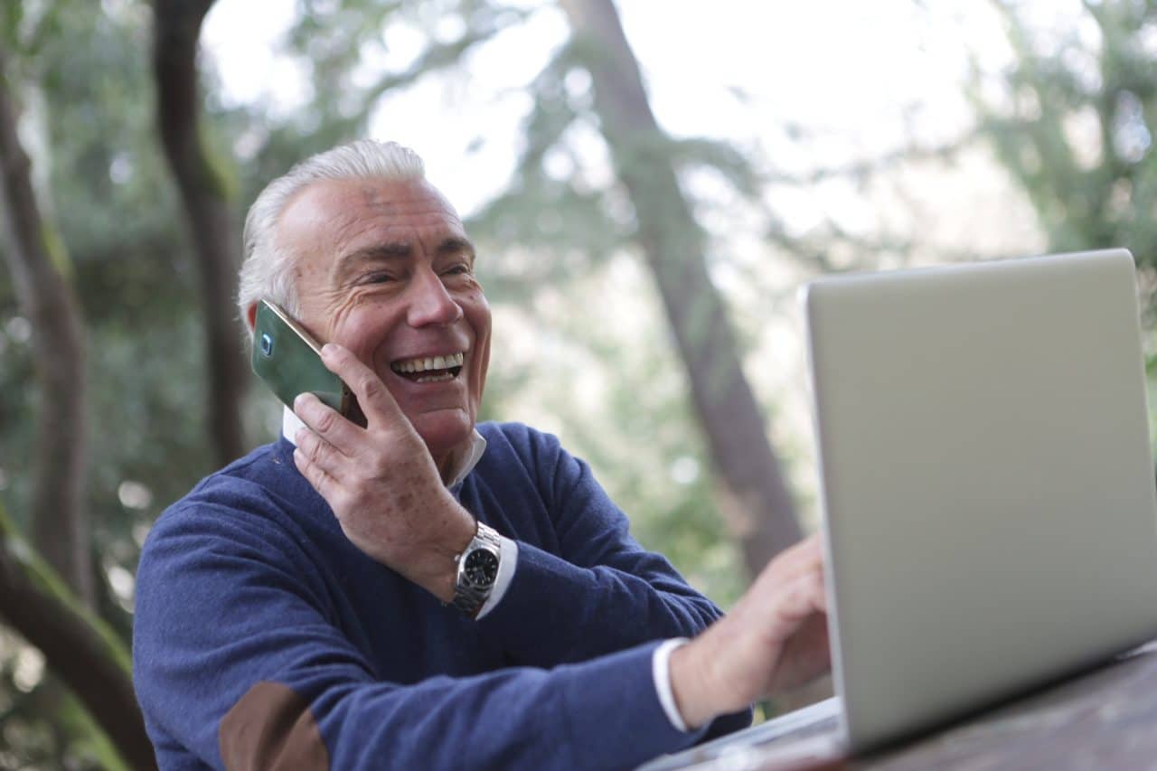 Senior man talking on a cell phone and working on his laptop.