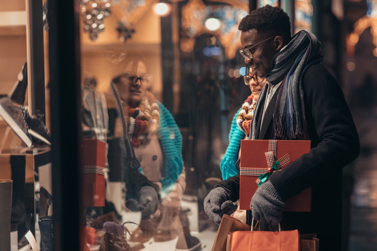 A couple looking through a shop window holding gifts.