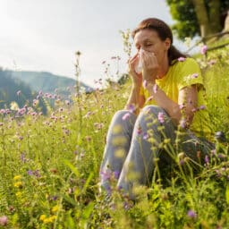 Woman sitting in a flower field blowing her nose