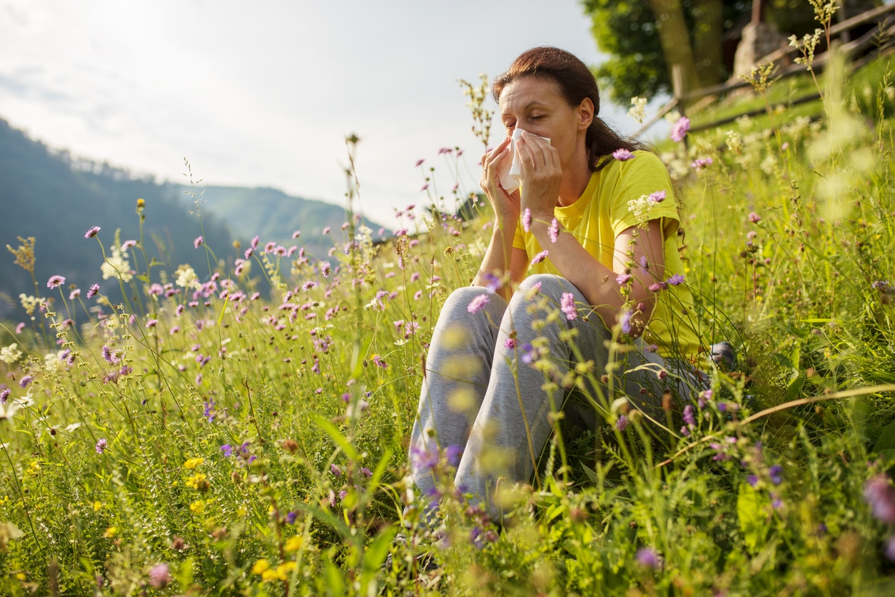 Woman sitting in a flower field blowing her nose