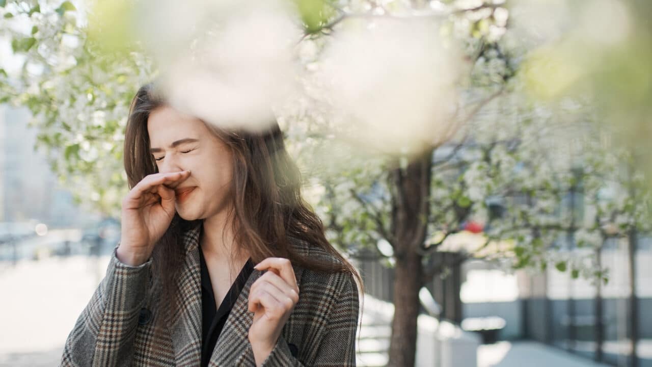 Woman scratching nose by trees