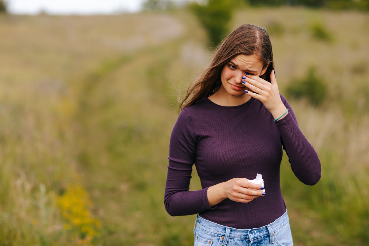 Woman with allergies rubs eyes in field