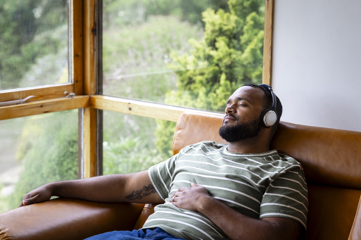 Man on a couch listening to music through her headphones.