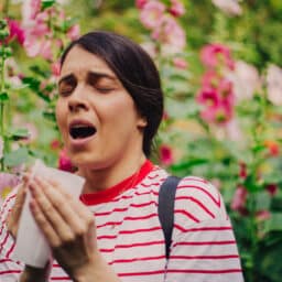 Woman sitting in a garden sneezing into a tissue